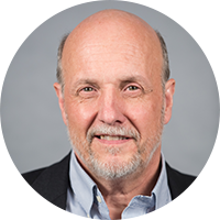 A photo of a White man with a white beard and mustache and thinning hair wearing a blue collared shirt and dark suit jacket