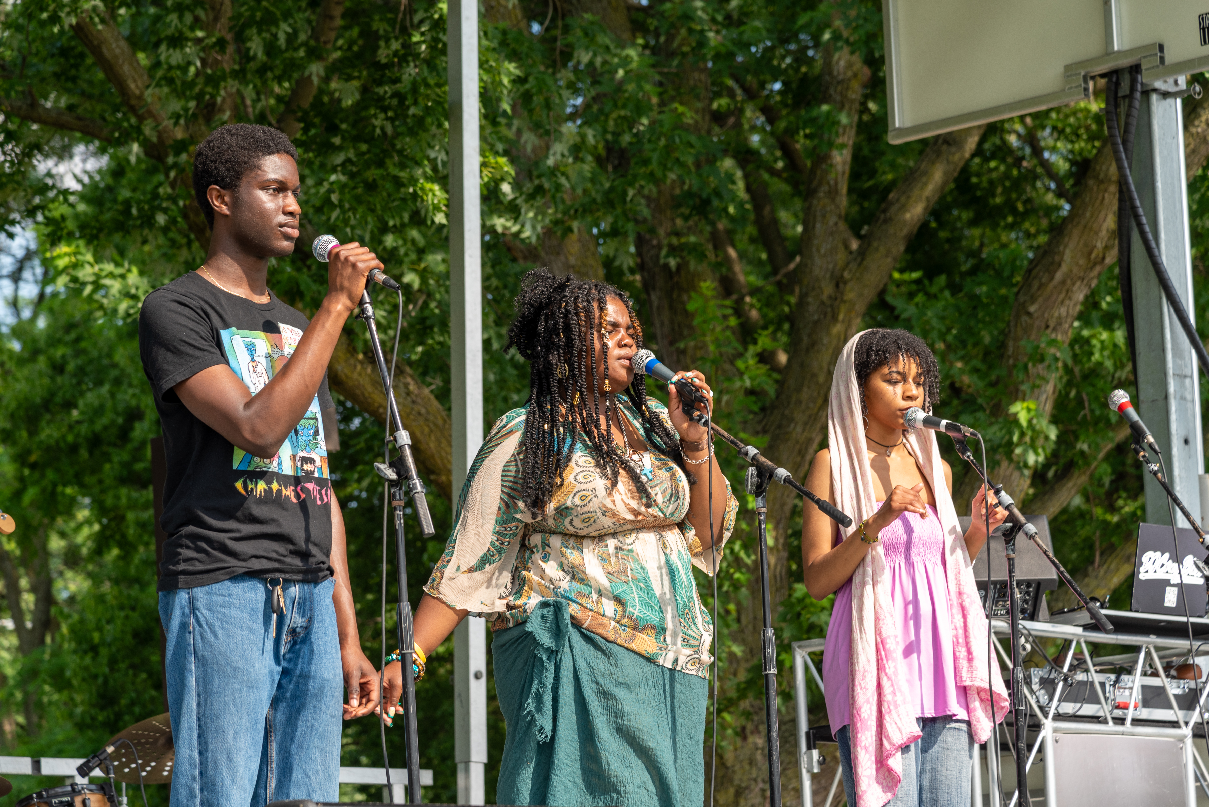 three people standing on an outdoor stage and singing