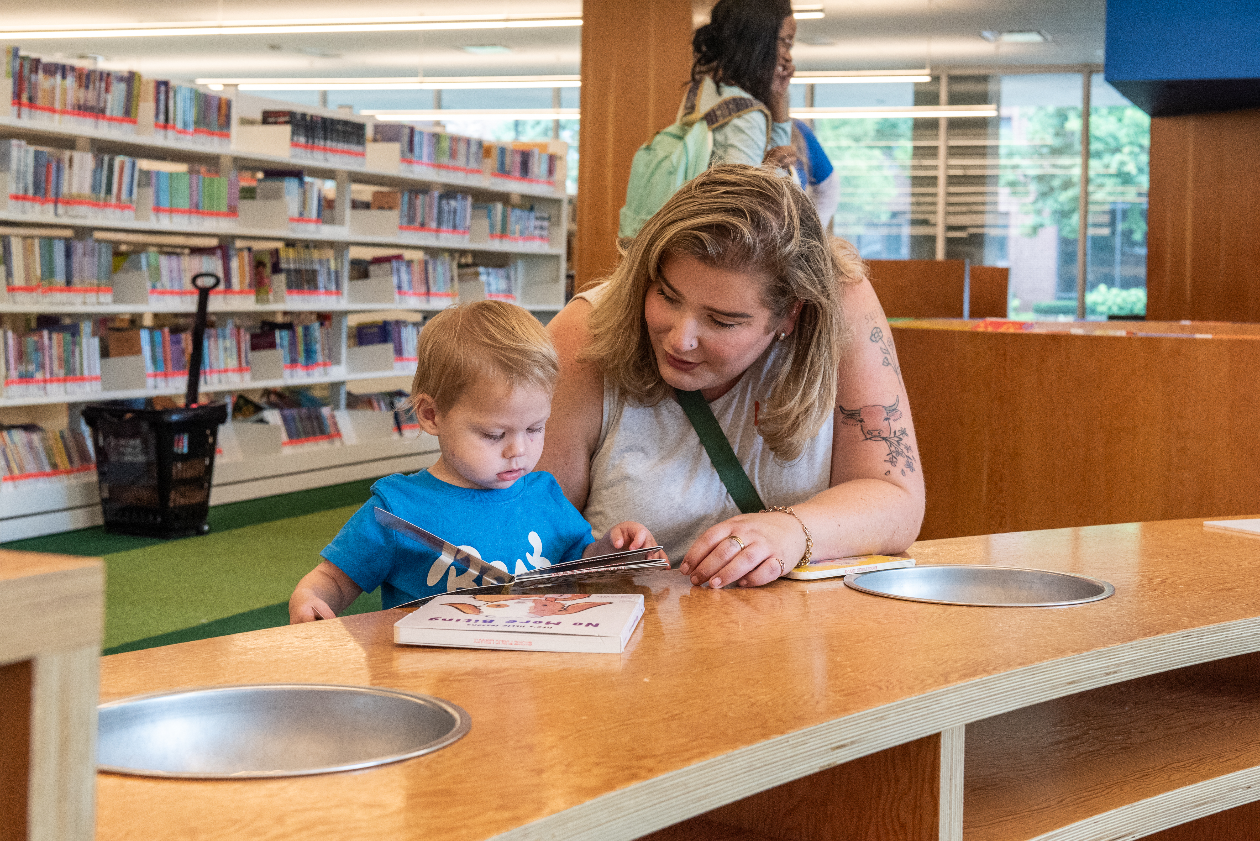 an adult woman is with a toddler looking at a board book in the library. 